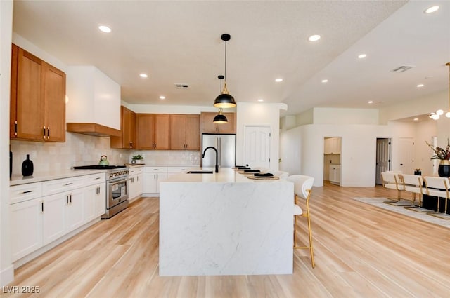 kitchen featuring pendant lighting, a sink, appliances with stainless steel finishes, light wood-style floors, and backsplash