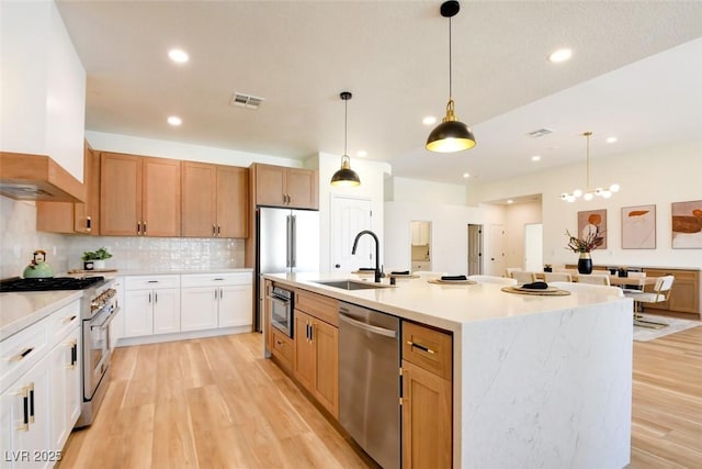 kitchen featuring light wood-style flooring, stainless steel appliances, a sink, visible vents, and premium range hood