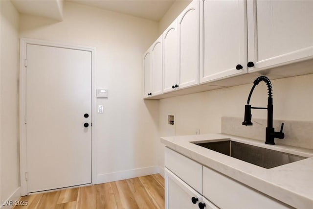 laundry area with cabinet space, a sink, light wood-style floors, washer hookup, and baseboards