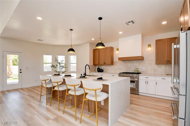 kitchen featuring tasteful backsplash, custom range hood, light countertops, high end range, and a center island with sink