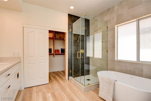 bathroom featuring recessed lighting, a shower stall, vanity, a freestanding bath, and wood finished floors