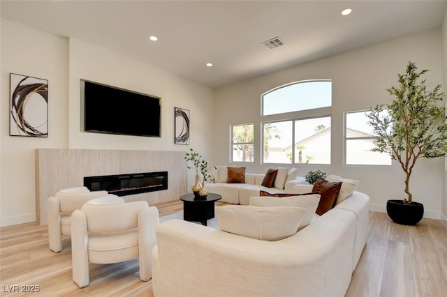 living room with a glass covered fireplace, visible vents, light wood-style flooring, and recessed lighting