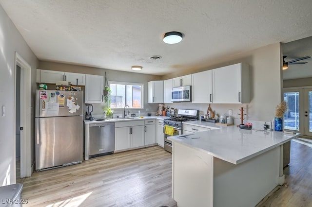 2129 N Michael Way, Las Vegas, NV 89108 - kitchen with stainless steel appliances, a peninsula, light wood-style floors, a textured ceiling, and light countertops