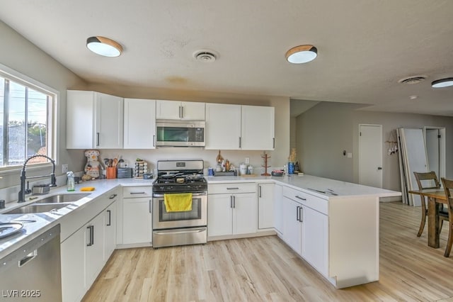 2129 N Michael Way, Las Vegas, NV 89108 - kitchen featuring stainless steel appliances, a peninsula, light countertops, light wood-style floors, and white cabinetry