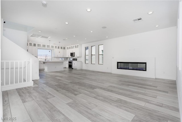 8125 Monsoon Bay St, Las Vegas, NV 89113 - unfurnished living room with light wood-style flooring, a sink, visible vents, a glass covered fireplace, and recessed lighting