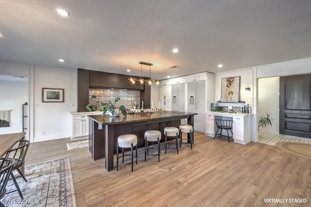 kitchen with a breakfast bar, white cabinets, a textured ceiling, and light wood-style flooring
