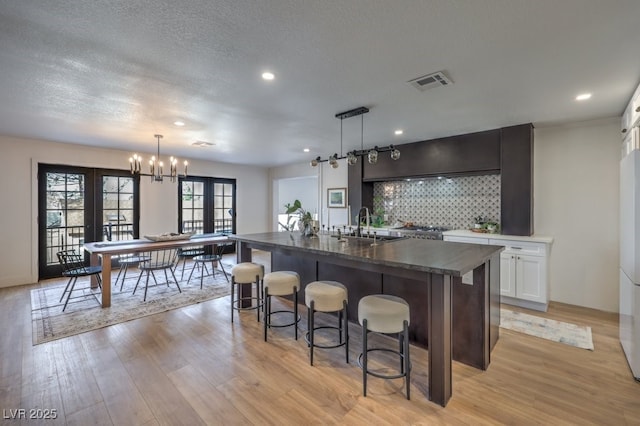 bar featuring tasteful backsplash, visible vents, a notable chandelier, and light wood finished floors