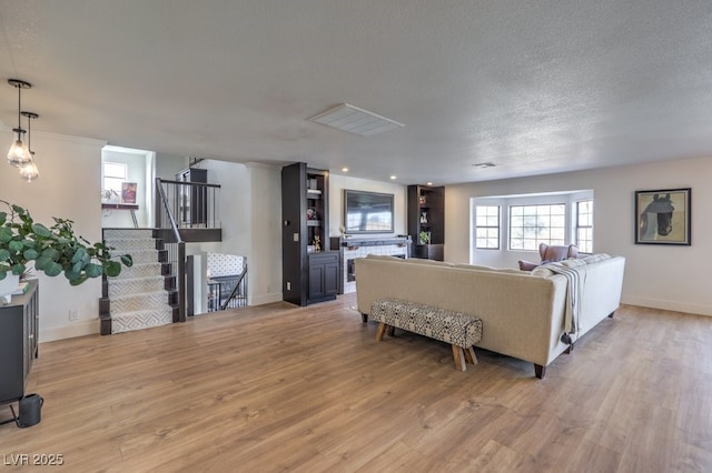 living area featuring stairway, light wood finished floors, a textured ceiling, and baseboards