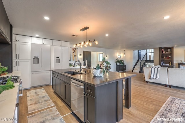 kitchen with a sink, premium appliances, dark countertops, open floor plan, and light wood-type flooring