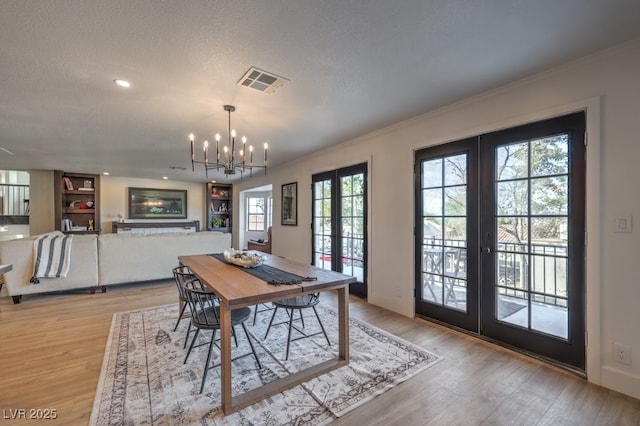 dining room with a chandelier, light wood-style floors, visible vents, a textured ceiling, and french doors