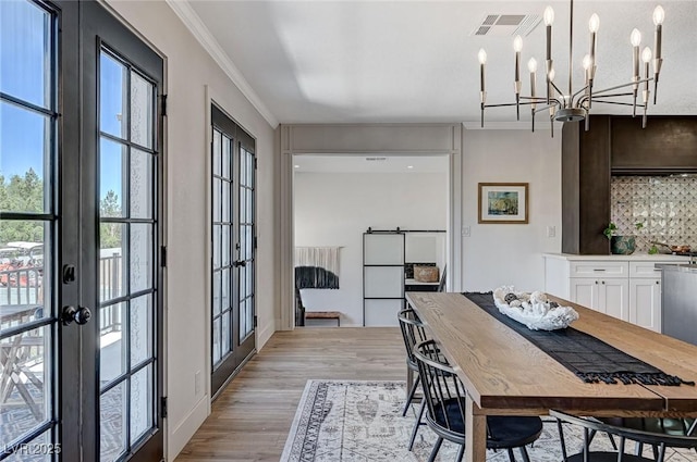 dining area featuring an inviting chandelier, light wood-style floors, visible vents, ornamental molding, and french doors