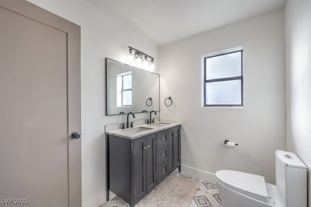 bathroom with toilet, double vanity, a sink, and baseboards