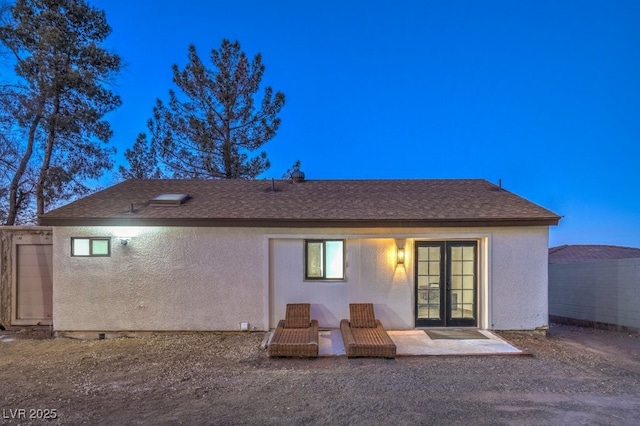 back of property with stucco siding, roof with shingles, a patio area, and french doors