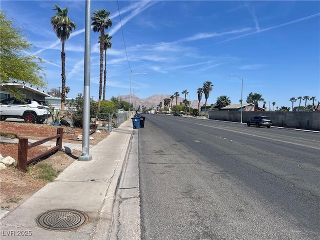 view of road featuring a mountain view, sidewalks, curbs, and street lights