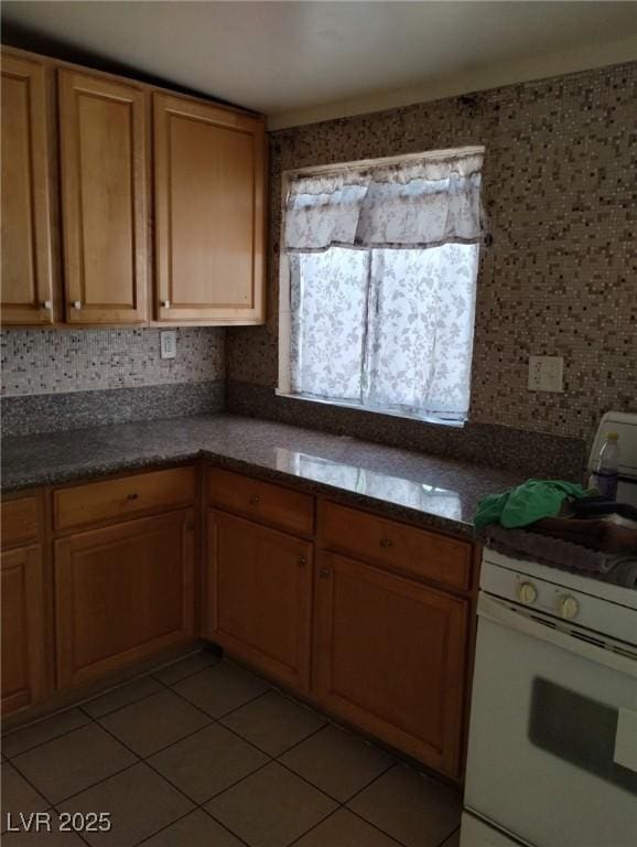 kitchen with gas range gas stove, brown cabinetry, dark countertops, and light tile patterned flooring