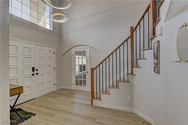 foyer entrance with a towering ceiling, stairs, wood finished floors, and baseboards