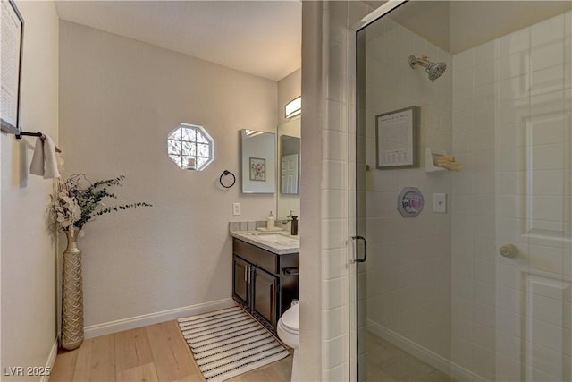 bathroom featuring wood finished floors, vanity, a stall shower, and baseboards