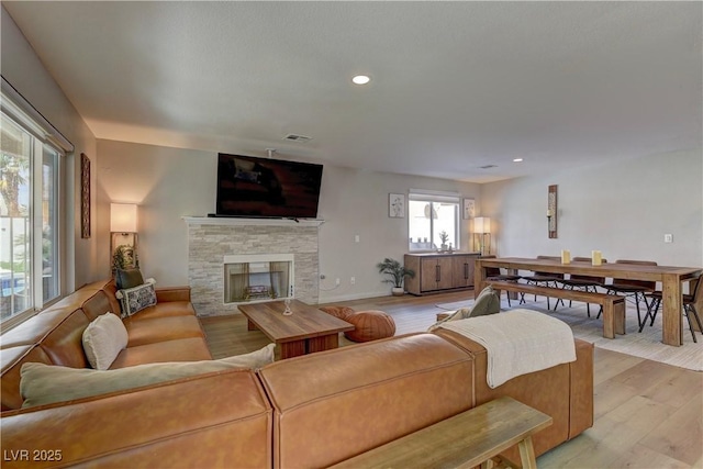 living area featuring recessed lighting, light wood-style floors, and a stone fireplace
