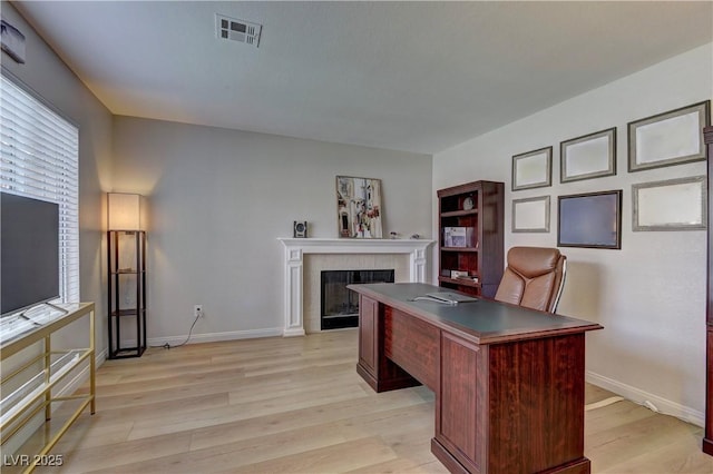 office space with a tile fireplace, visible vents, light wood-style flooring, and baseboards