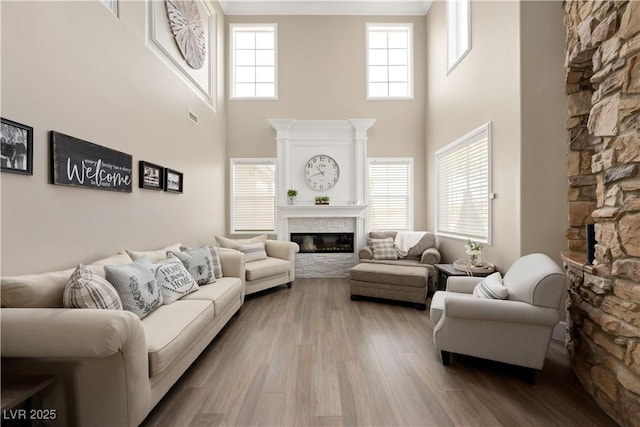 living area with wood finished floors, ornamental molding, a glass covered fireplace, visible vents, and a towering ceiling