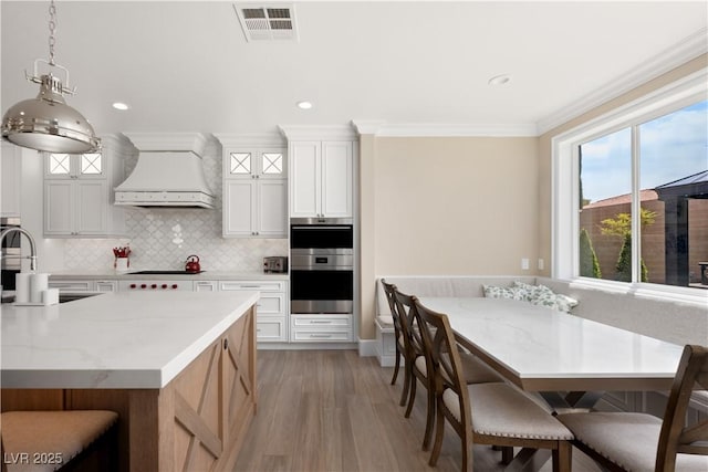 kitchen with a sink, decorative backsplash, visible vents, light wood-style flooring, and premium range hood