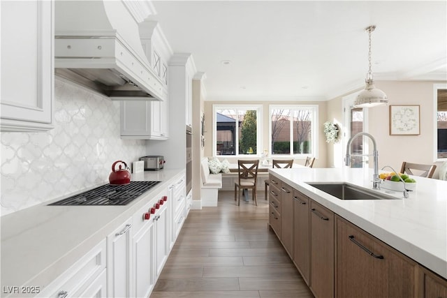 kitchen with gas stovetop, custom exhaust hood, light countertops, and a sink