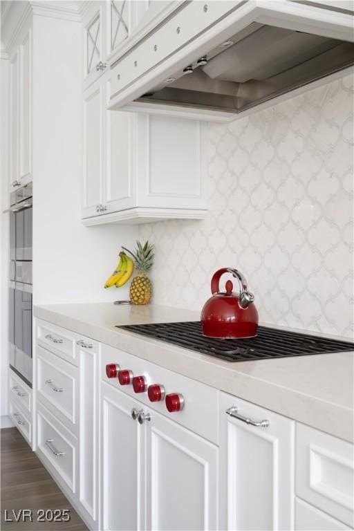 bar featuring tasteful backsplash, stovetop, under cabinet range hood, dark wood-type flooring, and multiple ovens