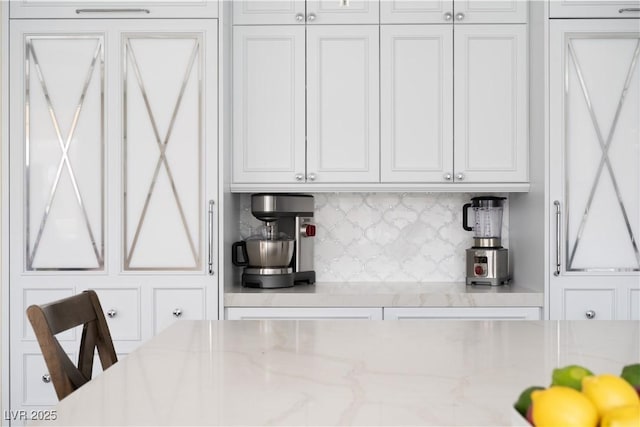 kitchen with light stone countertops, backsplash, and white cabinetry