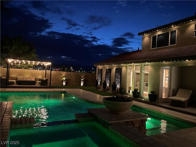 pool at night featuring a pool with connected hot tub, a fenced backyard, and a patio area