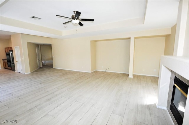 unfurnished living room featuring a raised ceiling, visible vents, light wood-style floors, a tiled fireplace, and a ceiling fan