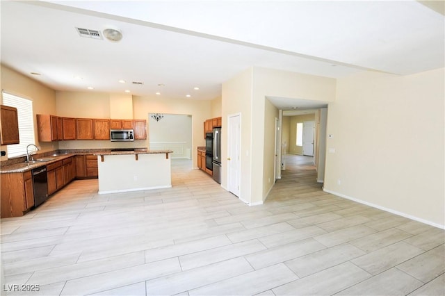 kitchen featuring brown cabinets, a sink, visible vents, stainless steel appliances, and a kitchen island