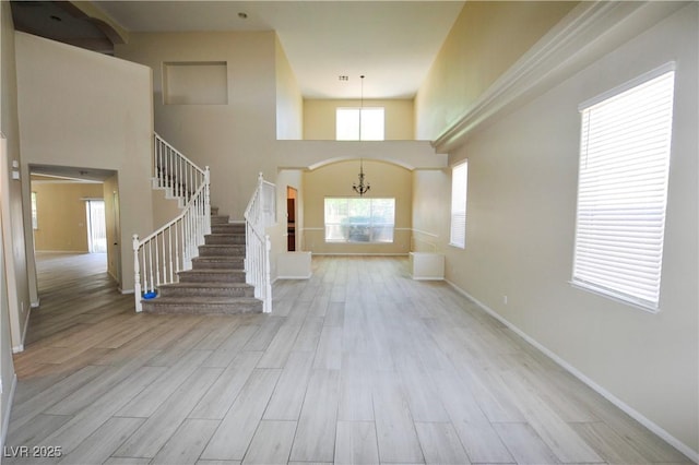 entrance foyer with a chandelier, stairs, baseboards, wood finished floors, and a high ceiling