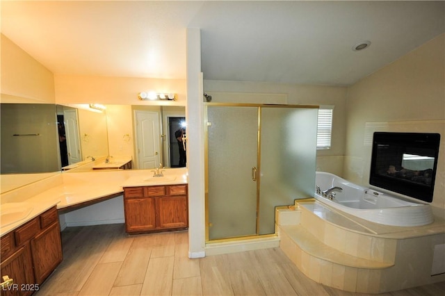 full bath with a shower stall, vanity, a glass covered fireplace, vaulted ceiling, and a garden tub