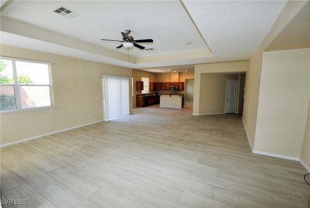 unfurnished living room featuring light wood-type flooring, baseboards, visible vents, a ceiling fan, and a tray ceiling