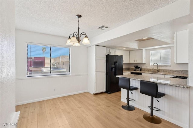 kitchen featuring black appliances, a sink, white cabinetry, visible vents, and a peninsula