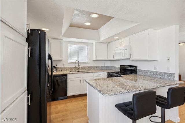 kitchen with white cabinets, black appliances, a sink, a raised ceiling, and a peninsula