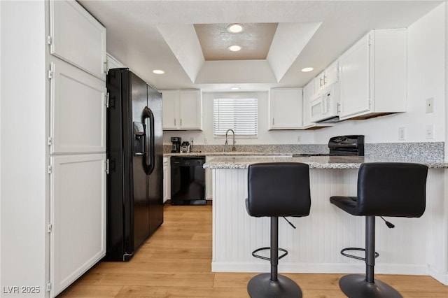 kitchen with light wood finished floors, black appliances, a breakfast bar, a peninsula, and white cabinetry