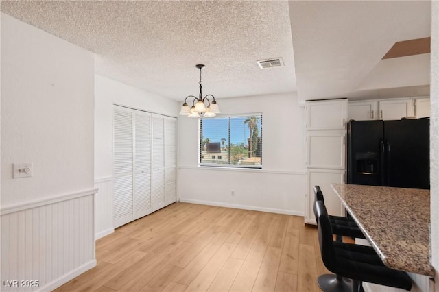 unfurnished dining area featuring visible vents, a notable chandelier, light wood-style floors, and a textured ceiling