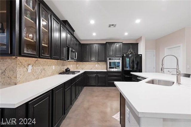 kitchen with appliances with stainless steel finishes, a sink, dark cabinets, decorative backsplash, and light countertops