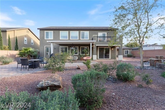 back of property featuring stucco siding, a balcony, a patio area, and fence