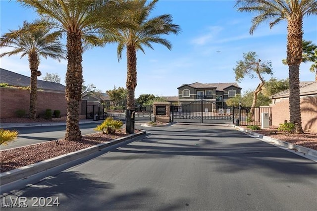 view of asphalt street with a gate, a gated entry, curbs, and a residential view