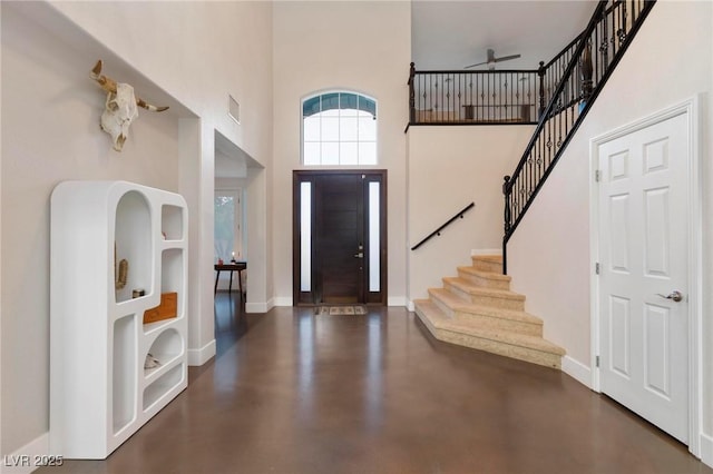 entryway featuring a towering ceiling, ceiling fan, stairs, concrete flooring, and baseboards