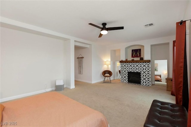 carpeted bedroom featuring a tiled fireplace, baseboards, and ceiling fan