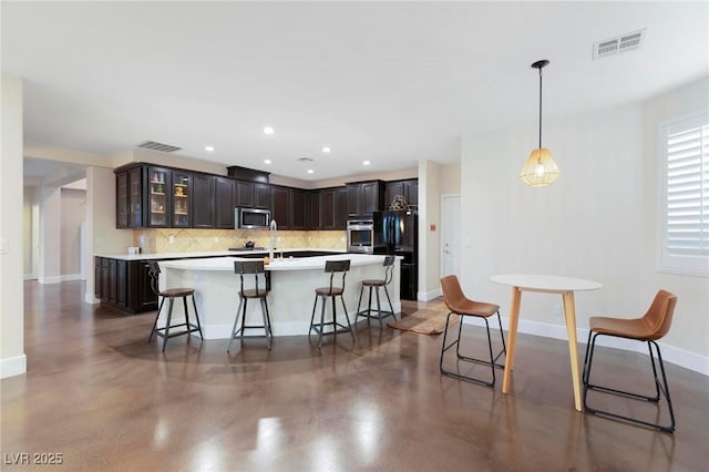 kitchen featuring stainless steel microwave, decorative backsplash, freestanding refrigerator, concrete flooring, and a breakfast bar