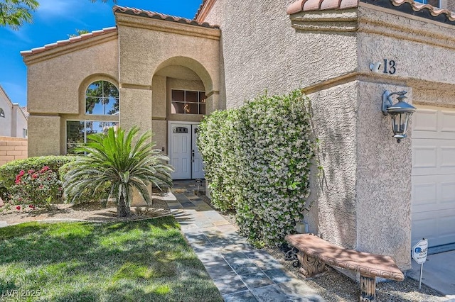 13 Cozy Glen Cir, Henderson, NV 89074 - view of exterior entry with a garage, a tiled roof, and stucco siding