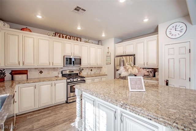1125 Via Canale Dr, Henderson, NV 89011 - kitchen with light wood finished floors, stainless steel appliances, visible vents, backsplash, and light stone counters
