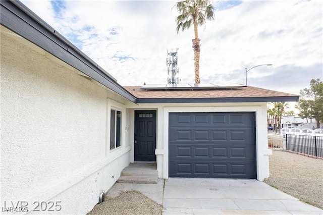entrance to property featuring a garage, driveway, solar panels, stucco siding, and fence