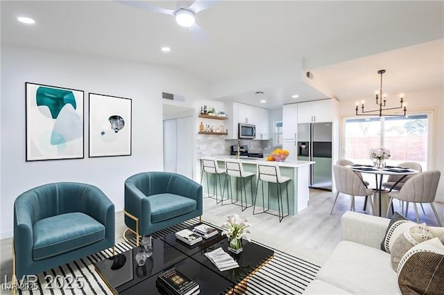 living area with recessed lighting, light wood-type flooring, visible vents, lofted ceiling, and ceiling fan with notable chandelier