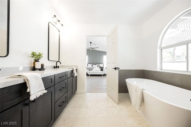 ensuite bathroom featuring a sink, double vanity, a freestanding tub, a ceiling fan, and ensuite bath