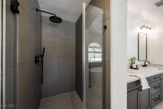 bathroom with a tile shower, a textured ceiling, visible vents, and vanity
